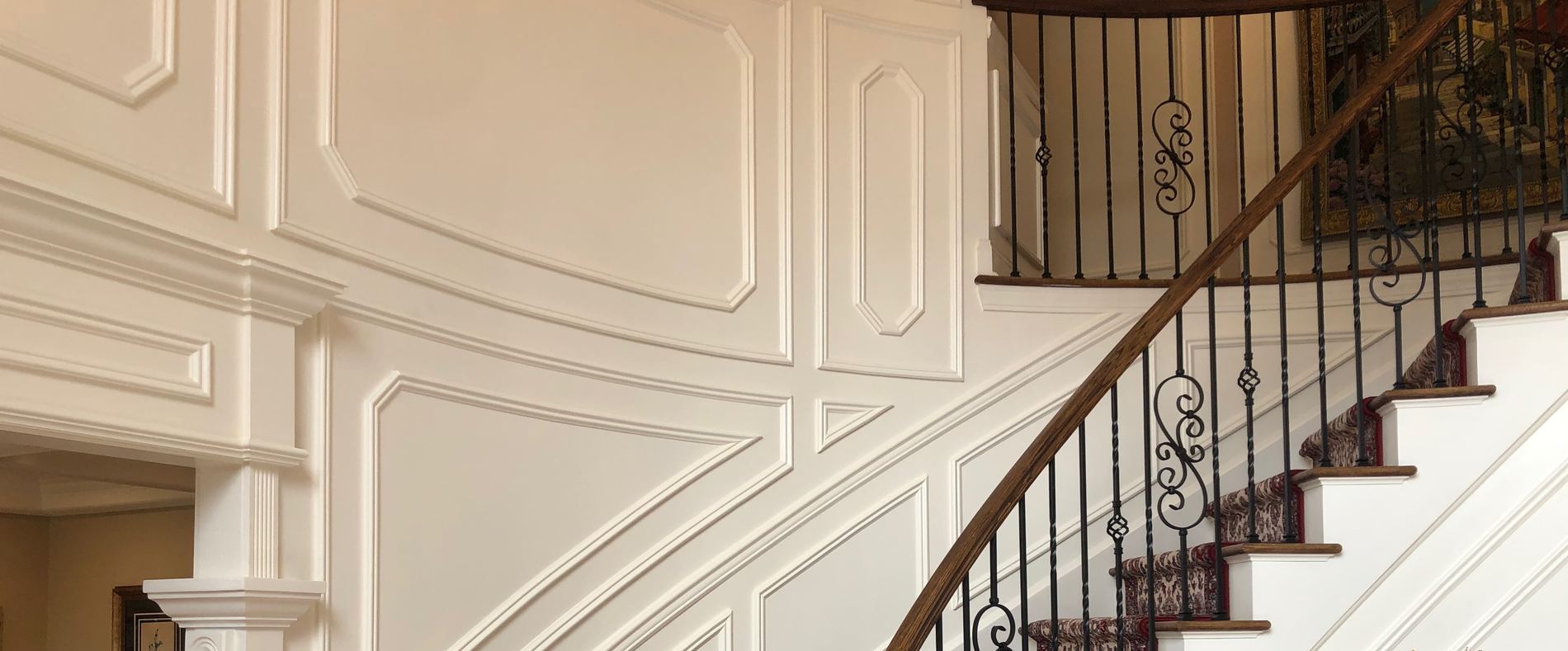Curved staircase with wainscoted wall and wrought iron railing by Doyle Renovations